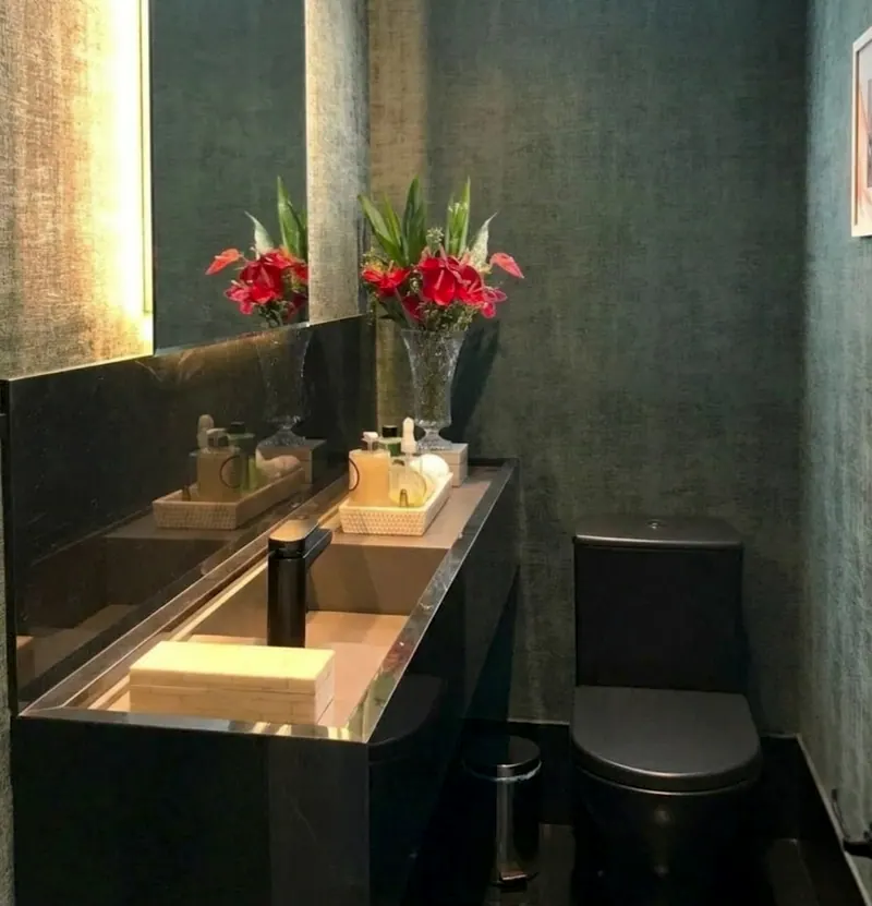 Lavabo escuro com bancada de pedra preta, cuba retangular, torneira preta e flores vermelhas